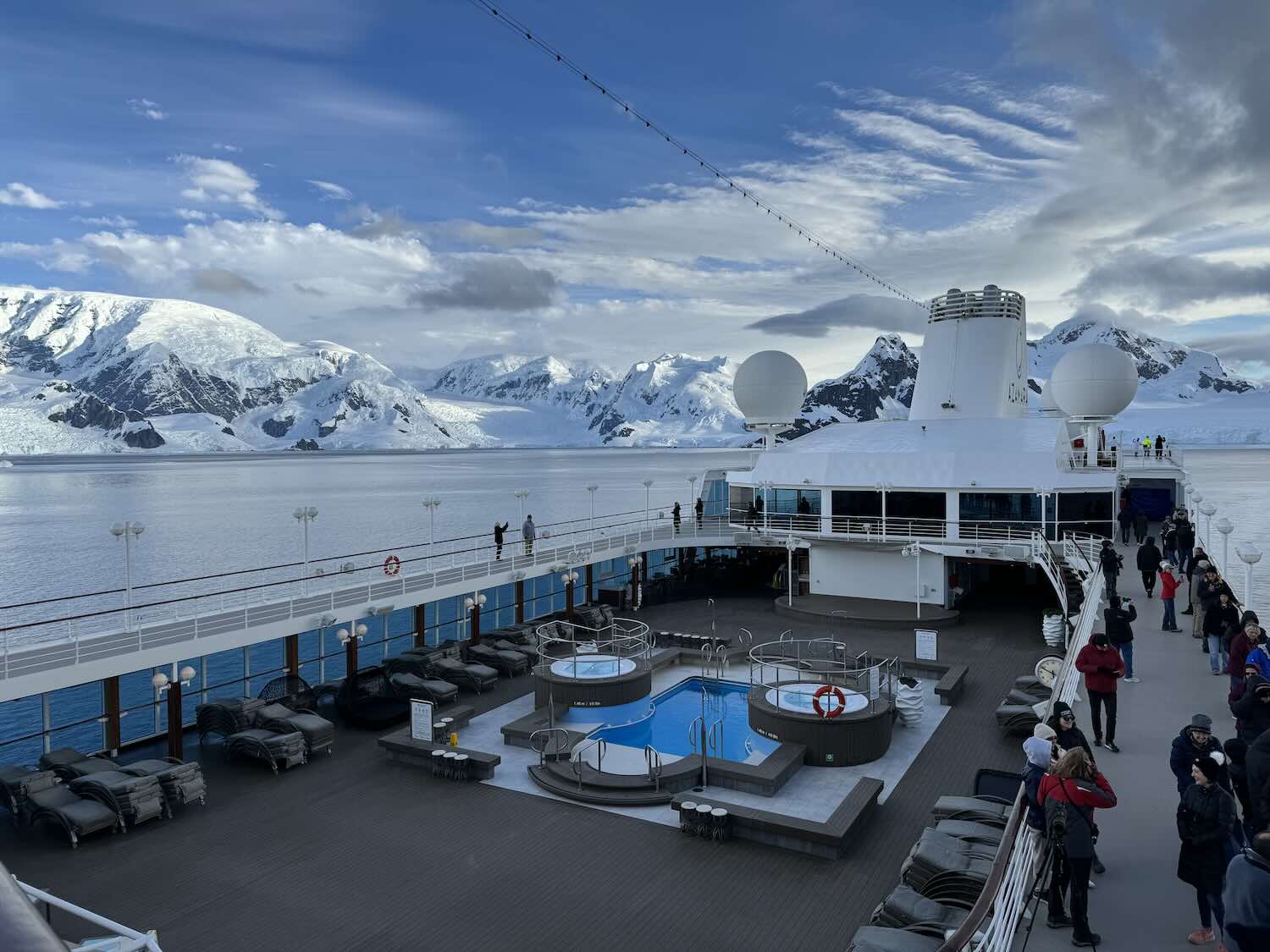 deck de navio com piscina e montanhas da antártida ao fundo.